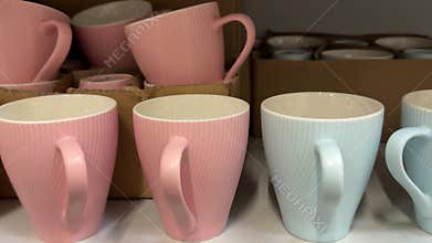 Pink ceramic mugs with white interiors displayed on retail shelves in a kitchenware store alongside blue cups featuring