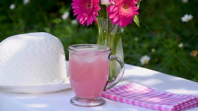 Pink lemonade in a clear mug with ice on a table with shadows created by leaves on the trees
