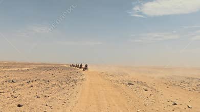 Convoy of Quad Bikes Driving Along Desert Road Raising Dust