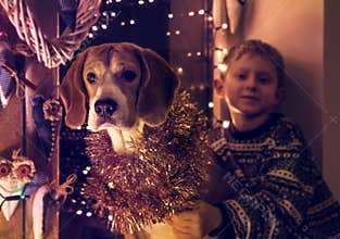 Little boy with his dog sitting on the decorated window for Christmass Eve