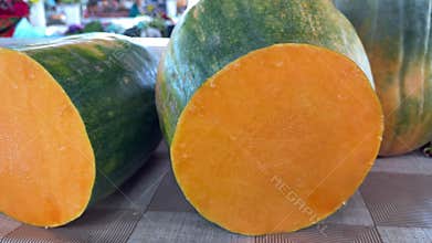 Fresh pumpkin cut in half with bright orange flesh displayed at farmers market showing seasonal vegetable harvest ready