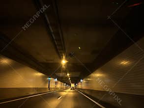 Nighttime road inside illuminated traffic tunnel with single car driving ahead