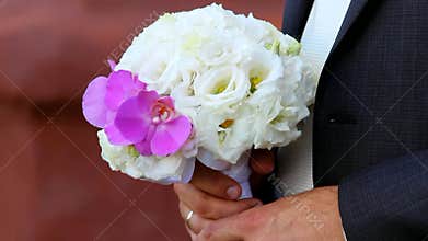 Beautiful wedding bouquet of white roses and pink orchids for bride in hands of bridegroom