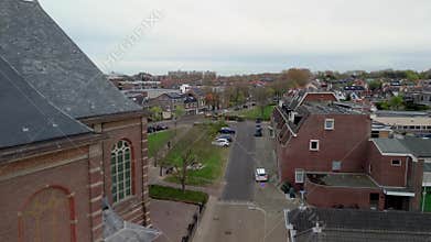 An aerial view shows a cozy European town street with traditional red-tiled roofs and a large brick church. Typical Dutch