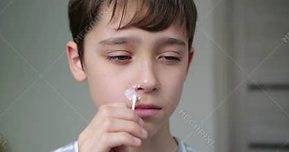 Child applying skincare treatment for blemish. Young boy focuses on hygiene routine at home. Healthcare and hygiene