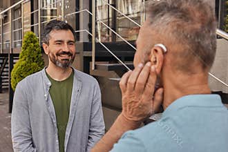 Senior man with a hearing impairment uses a hearing aid to communicate