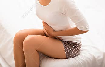 Woman suffering from stomach pain, sitting on bed.