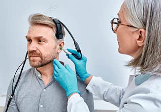 Experienced audiologist with tympanometer probe does tympanometry procedure and impedance audiometry for adult male patient at