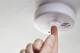 Close Up Of Hand Testing Domestic Smoke Alarm