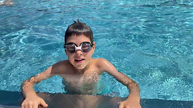 Smiling boy in goggles talking directly to camera in swimming pool