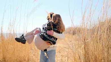 Man carries girlfriend through tall grass by the lake, savoring spring warmth.