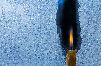 Closeup of little candle flame behind frozen window glass