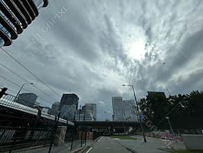 Modern office towers rise above urban roadways under dramatic cloudy sky, with