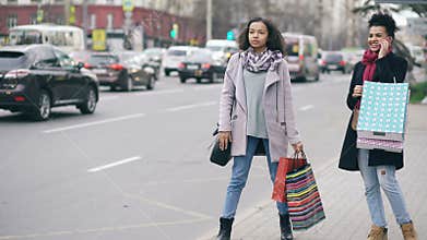 Two attractive african american women with shopping bags calling for taxi cab while coming back from mall sales