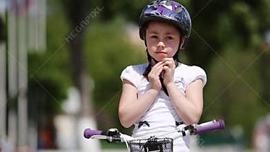Close-up of the girl wearing helmet and then rides a bicycle in the city park.