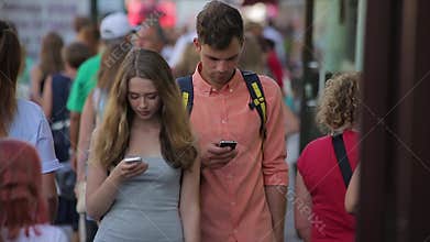 Young couple stroll along the busy city street and look at their mobiles in slo-mo