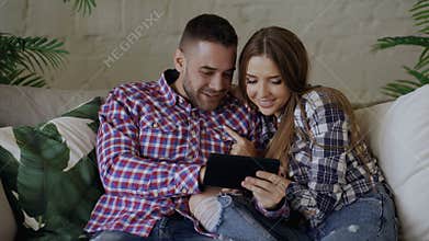Young attractive couple using tablet computer for surfing internet and chatting sit on couch in living room at home