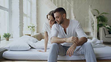 Depressed yong man sitting in bed having stressed while his girlfriend come and embrace him and kiss in bedroom at home