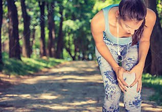Female athlete runner touching knee in pain, fitness woman running in park.