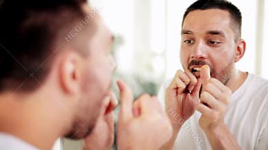Man with dental floss cleaning teeth at bathroom