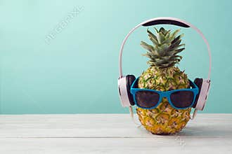 Pineapple with headphones and sunglasses on wooden table over mint background. Tropical summer vacation and beach party.