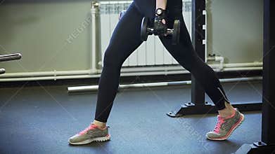 Close up shot of a woman who does warm-up squats with dumbbells.