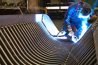 Welder in a factory, repairing a steel blade of a bulldozer