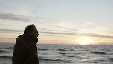 Young man walking in the shore of the sea alone and looking on the waves. Male enjoying the sunset on the beach.