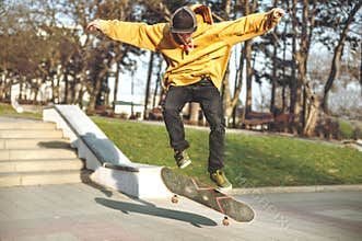 The teenager in a sweatshirt and a cap jumps with a board in the city against the backdrop of the urban sunset light