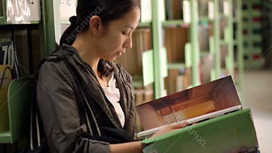 Student girl sitting beside bookshelves and reading books