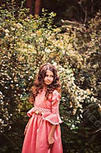 Summer portrait of curly smiling child girl in pink fairytale princess dress in the forest