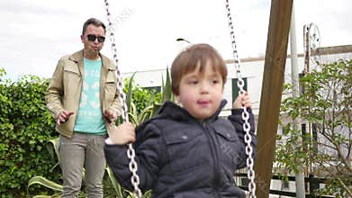 Dad Pushing her Baby in the Park Swing