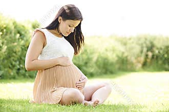 Pregnant Woman Sitting On Grass Outdoors Holding Bump