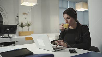A woman working at the computer and drinking orange juice