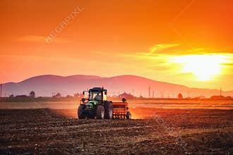 Beautiful sunset, farmer in tractor preparing land with seedbed