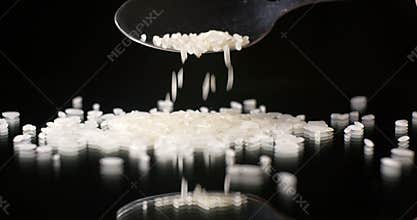 Raw rice grain falling on reflective table top on black background