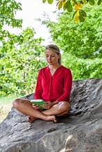 Smiling 20s girl reading a summer book under a tree