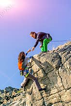 Two climbers reaching summit one holding hand of