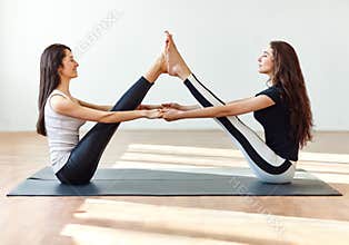 Two young women doing yoga asana buddy boat pose