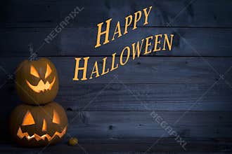 Two Cute Lighted Pumpkins with Happy Halloween Written on a Dark Blue Rustic Wood Board Background