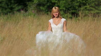 Lovely gentle blonde bride dancing in a wheat field in white bridal dress