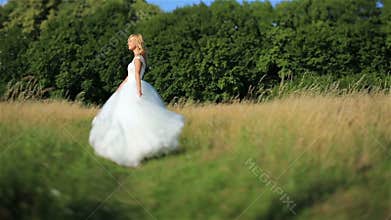 Beautiful romantic stylish blonde bride in white dress dancing in the green field in the sun