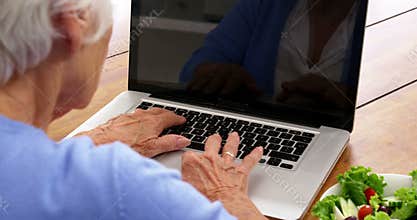 Close up mature woman using a laptop with a salad putting on the table