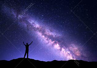 Night colorful landscape with purple Milky Way and silhouette of a standing sporty man with raised up arms on the mountain