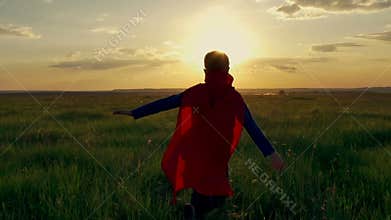 Boy superhero in a field at sunset