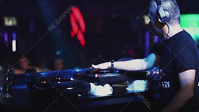 Dj spinning at turntable on party in nightclub. Crowd of dancing people.