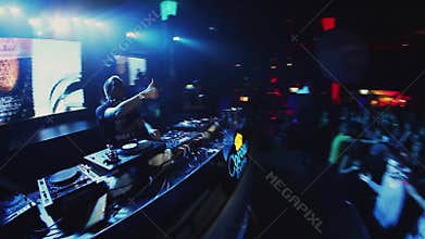 Dj spinning and dancing at turntable on party in nightclub. Illuminations. Crowd