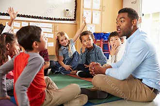 Elementary school kids and teacher sit cross legged on floor