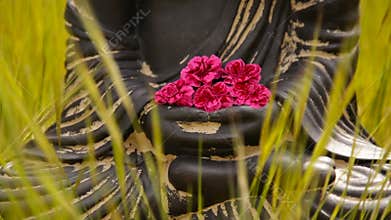 Close up of buddha figurine with red flowers in the middle of green meadow