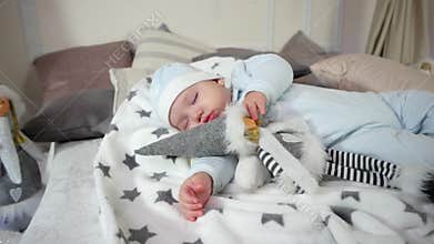 Baby lying on the bed in the sliders and cap, sweet dream cute boy, child hugging a toy while sleeping, Small child